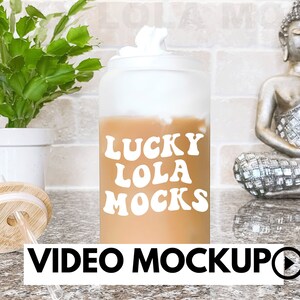 Puede incluir: Un vaso de vidrio esmerilado con tapa blanca y una pajita. El vaso está lleno de un líquido marrón claro y tiene el texto "LUCKY LOLA MOCKS" impreso en blanco en el lateral.