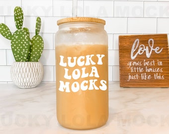 Può includere: Un barattolo di vetro trasparente con un coperchio in bambù e un adesivo in vinile bianco che dice "LUCKY LOLA MOCKS" in un font retrò. Il barattolo è pieno di un liquido marrone chiaro e si trova su un bancone bianco. Un cartello in legno con il testo "love grows best in little houses just like this" è sullo sfondo.