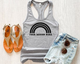 Op de afbeelding: Een grijze tanktop met een zwart regenboogontwerp en de tekst "YOUR DESIGN HERE". De afbeelding bevat ook oranje sandalen en een spijkerbroek met zonnebril.