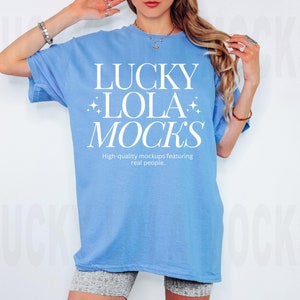 May include: A light blue t-shirt with the text "LUCKY LOLA MOCKS" in white. The text is surrounded by small white stars. The text below the main text reads "High-quality mockups featuring real people."
