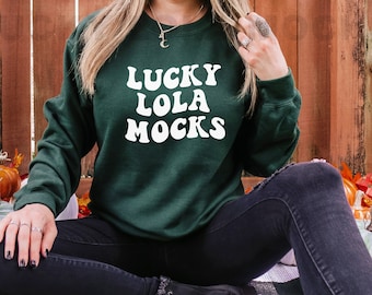 May include: A dark green sweatshirt with the text "LUCKY LOLA MOCKS" in white retro-style lettering.