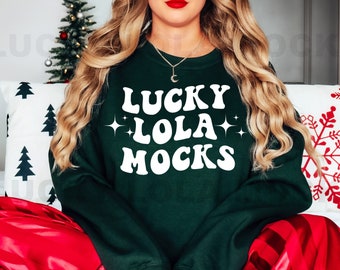 May include: A green sweatshirt with the text "Lucky Lola Mocks" in white. The model is wearing the sweatshirt with red satin pants.