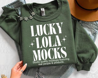 May include: A dark green sweatshirt with the text "LUCKY LOLA MOCKS" in white. The sweatshirt is paired with blue jeans and a brown hat. The text below reads "Studio quality mockups featuring real people & products."