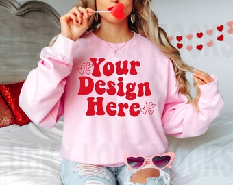 Puede incluir: Una sudadera rosa con el texto "Your Design Here" en letras rojas. La sudadera tiene cuello redondo y mangas largas. La modelo lleva la sudadera con unos pantalones cortos de mezclilla desgarrados.