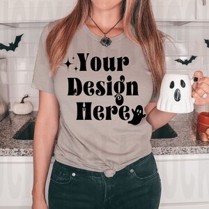 May include: A woman wearing a light gray t-shirt with the text "Your Design Here" in black. She is holding a white ghost-shaped mug.