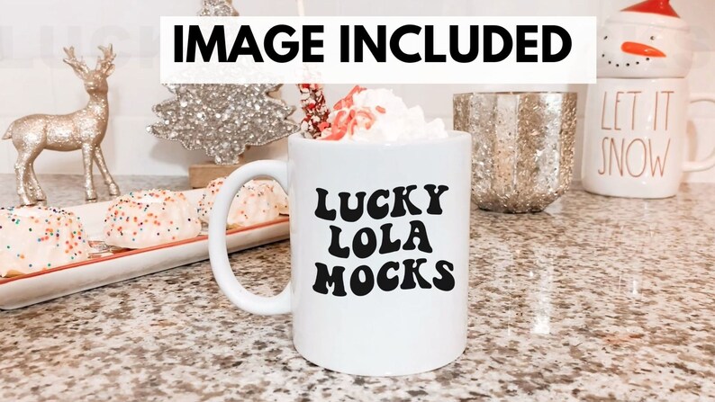 May include: White ceramic mug with black text that reads "LUCKY LOLA MOCKS". The mug is filled with a white beverage topped with whipped cream. The mug is on a countertop with a festive background.