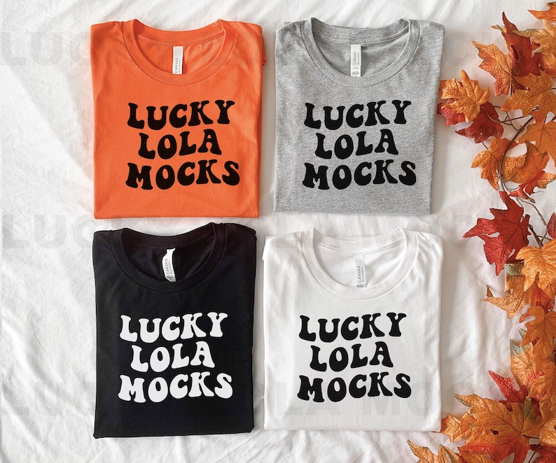 May include: Four t-shirts with the text "Lucky Lola Mocks" in black and white lettering on different coloured shirts. The shirts are orange, grey, black, and white.
