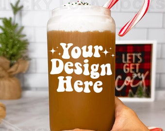 Puede incluir: Un vaso reutilizable marrón con una tapa blanca y crema batida blanca en la parte superior. El vaso tiene el texto "Your Design Here" en letras blancas. Un bastón de caramelo sobresale de la parte superior del vaso.