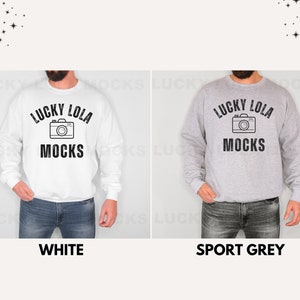 May include: A white sweatshirt with black text that reads "Lucky Lola Mocks" and a camera graphic. The sweatshirt is also available in sport grey.