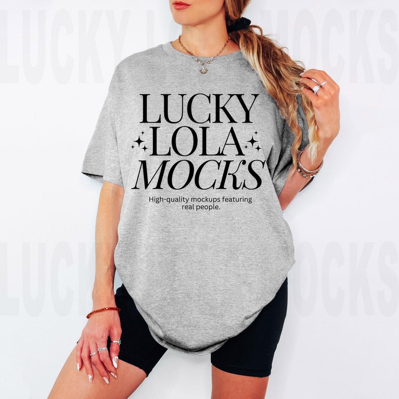 Puede incluir: Una camiseta gris de gran tama&ntilde;o con el texto "LUCKY LOLA MOCKS" en negro. El texto est&aacute; rodeado de peque&ntilde;as estrellas. Debajo del texto est&aacute; la frase "High-quality mockups featuring real people."