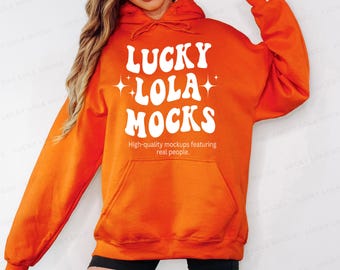 Puede incluir: Sudadera con capucha de color naranja brillante con bolsillo delantero y capucha con cordón. La sudadera presenta el texto "LUCKY LOLA MOCKS" en blanco, con la leyenda "High-quality mockups featuring real people."