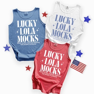 May include: Three tank tops in blue, white, and red, each with the text "LUCKY LOLA MOCKS" in white. The image includes star-shaped decorations and a small American flag, suggesting a patriotic theme. The text "Studio quality mockups featuring real people & products" is also visible.
