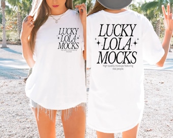 Op de afbeelding: Wit t-shirt met de zwarte tekst "LUCKY LOLA MOCKS" en sterren. De tekst "High-quality mockups featuring real people" staat eronder. Het t-shirt wordt door een persoon gedragen.