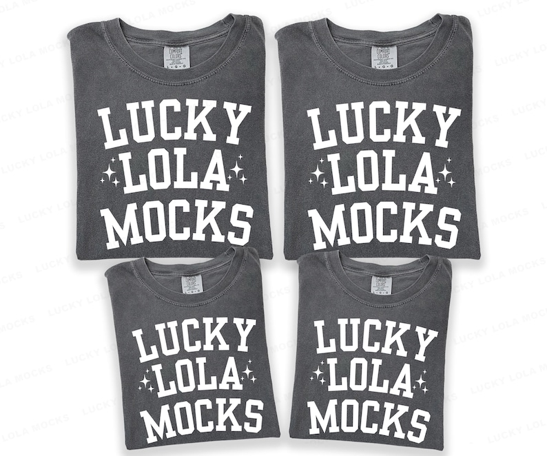 May include: Four gray t-shirts with the text "LUCKY LOLA MOCKS" in white block letters. The text includes star accents. The shirts are folded and stacked, showcasing the design on the front.