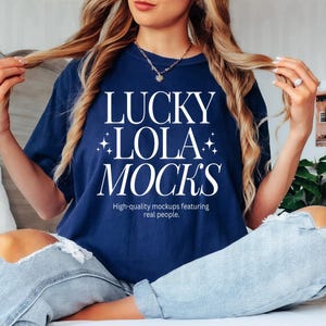 Pode incluir: Uma mulher vestindo uma camiseta azul marinho com o texto "LUCKY LOLA MOCKS" e as palavras "High-quality mockups featuring real people." A mulher está sentada em uma cama com as pernas cruzadas e está segurando o cabelo com uma mão.