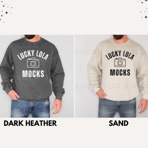 May include: Two sweatshirts with the text "Lucky Lola Mocks" and a camera graphic. The sweatshirt on the left is dark heather grey and the sweatshirt on the right is sand.