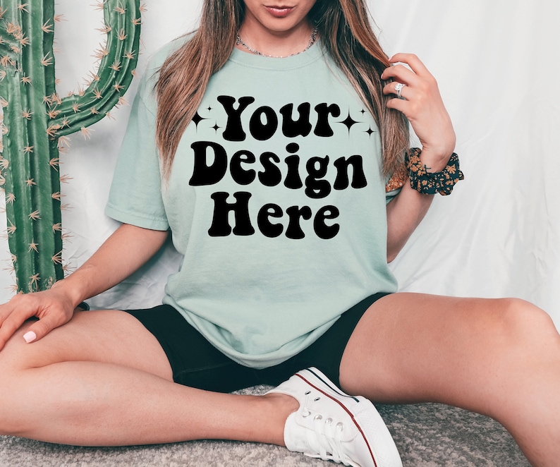 May include: A light blue t-shirt with the text "Your Design Here" in black retro-style lettering.