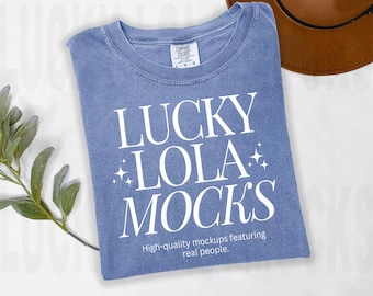 May include: A light blue t-shirt with the text "LUCKY LOLA MOCKS" in white. The text is surrounded by small white stars. The shirt has a distressed look and the text "High-quality mockups featuring real people." is printed below the main text.