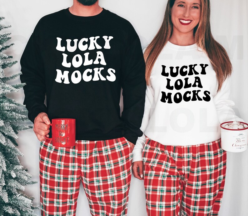 Puede incluir: Una pareja lleva sudaderas a juego en blanco y negro con el texto "Lucky Lola Mocks" en una fuente retro. Ambos llevan pantalones de pijama a cuadros rojos y verdes.