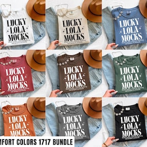 May include: A selection of t-shirts in different colours, each printed with the text "LUCKY LOLA MOCKS" in a prominent white font. The shirts are presented with denim jeans and a brown hat, suggesting a relaxed, everyday aesthetic. The text "COMFORT COLORS 1717 BUNDLE" is at the bottom.