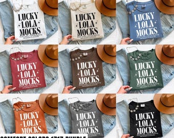 May include: A collection of t-shirts in various colors, each displaying the text "LUCKY LOLA MOCKS" in a bold, white font. The shirts are paired with denim jeans and a brown hat, showcasing a casual, everyday style. The text "COMFORT COLORS 1717 BUNDLE" is at the bottom.