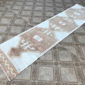 May include: A white and beige runner rug with a geometric pattern. The rug has a distressed look and is made of a soft, woven material.
