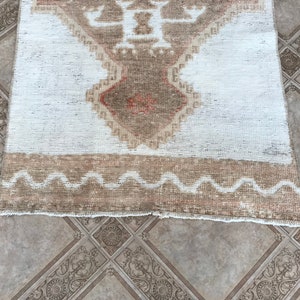 May include: A white and brown vintage rug with a geometric pattern. The rug has a fringe border and a wavy design along the bottom edge.