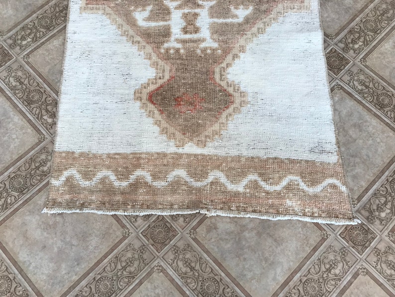 May include: A white and brown vintage rug with a geometric pattern. The rug has a fringe border and a wavy design along the bottom edge.
