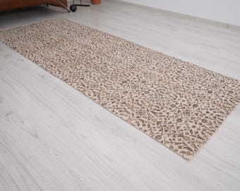 May include: A rectangular beige rug with a repeating floral pattern in shades of brown and tan. The rug is long and narrow, suitable for a hallway or entryway. The design is intricate and detailed, adding a touch of elegance to any space.
