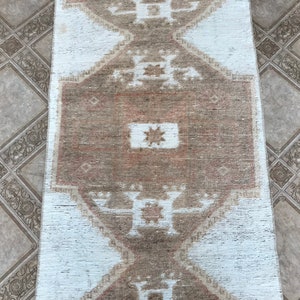 May include: A white and brown patterned rug with a geometric design. The rug has a faded, vintage look.
