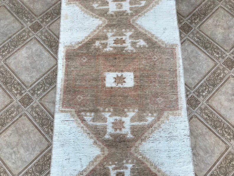 May include: A white and brown patterned rug with a geometric design. The rug has a faded, vintage look.