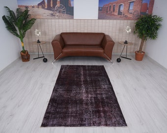 Puede incluir: Una alfombra vintage de color morado oscuro con un aspecto desgastado, colocada delante de un sofá de cuero marrón en un salón.