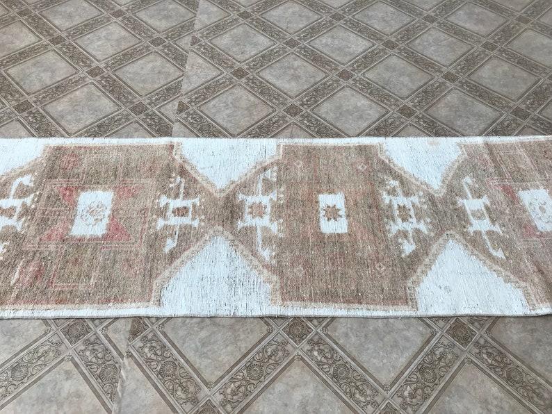 May include: A white and brown patterned runner rug with a geometric design. The rug has a distressed look and is made of natural fibers.