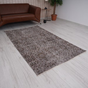May include: A vintage-style rug with a faded floral pattern in shades of brown and beige. The rug is laid out on a light wood floor.