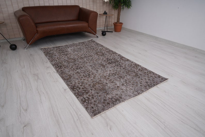 May include: A vintage-style rug with a faded floral pattern in shades of brown and beige. The rug is laid out on a light wood floor.