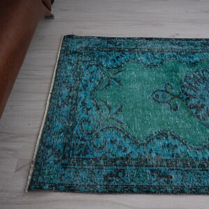 May include: A vintage teal and blue rug with a floral pattern. The rug has a distressed look and is made of a soft, woven material.