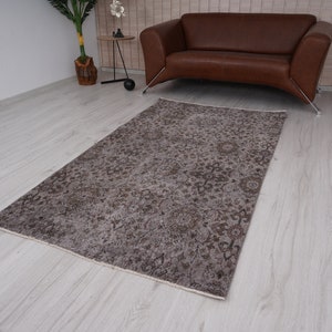 May include: A vintage-style rug with a faded floral pattern in shades of brown and beige. The rug is laid out on a light wood floor.
