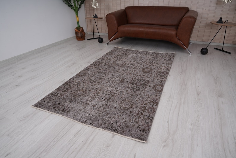 May include: A vintage-style rug with a faded floral pattern in shades of brown and beige. The rug is laid out on a light wood floor.