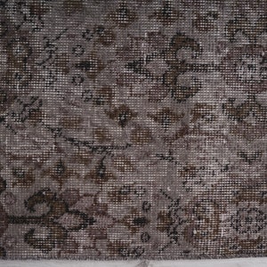 May include: A close-up of a brown and grey patterned rug with a subtle floral design. The rug has a distressed, vintage look.