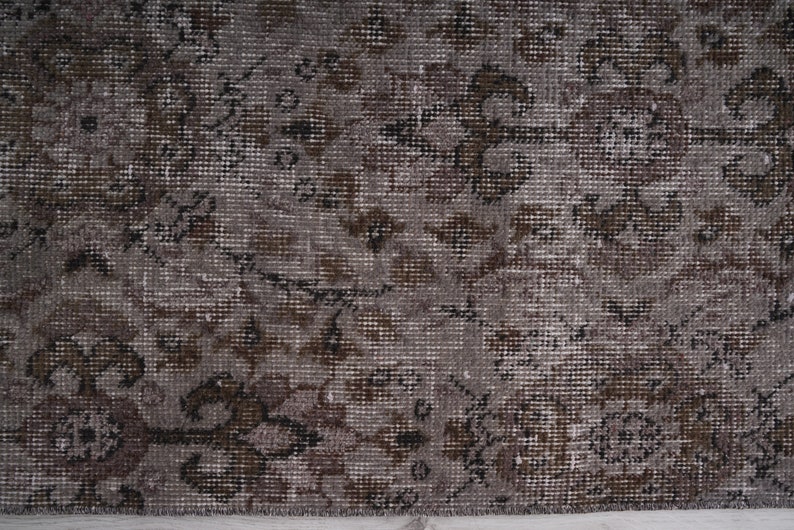 May include: A close-up of a brown and grey patterned rug with a subtle floral design. The rug has a distressed, vintage look.