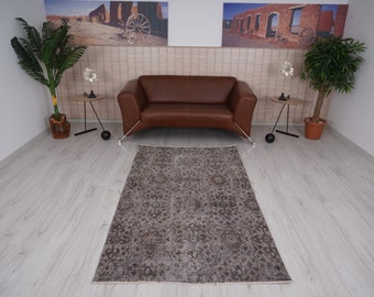 Puede incluir: Una alfombra marrón con estampado y aspecto desgastado, colocada delante de un sofá de cuero marrón en un salón.