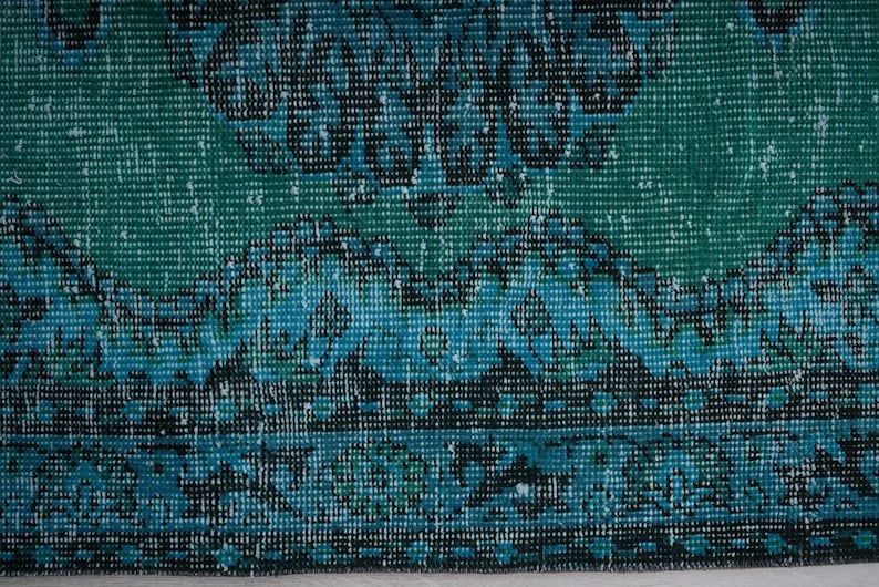 May include: Close-up of a blue and green patterned rug with a textured woven design.