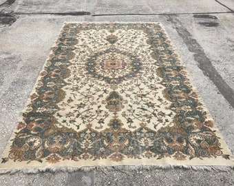 May include: A vintage cream-colored rug with a floral pattern in shades of brown, green, and pink. The rug has a fringed edge.