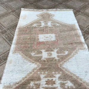 May include: A white and beige patterned rug with a geometric design. The rug has a faded, vintage look.