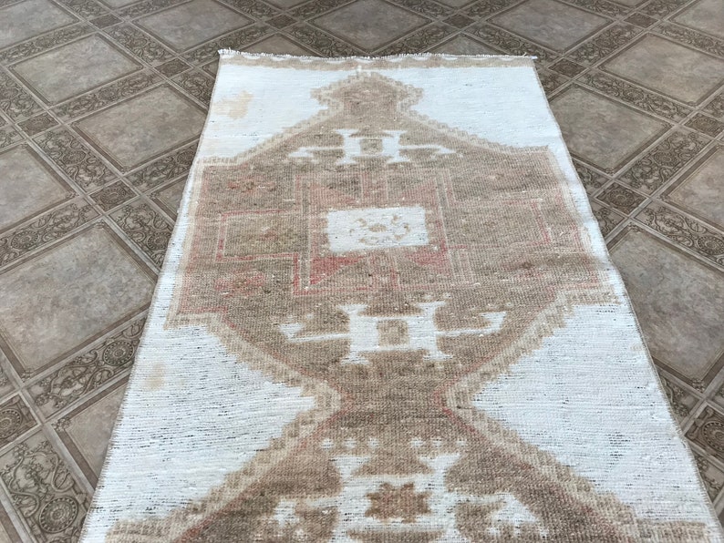 May include: A white and beige patterned rug with a geometric design. The rug has a faded, vintage look.