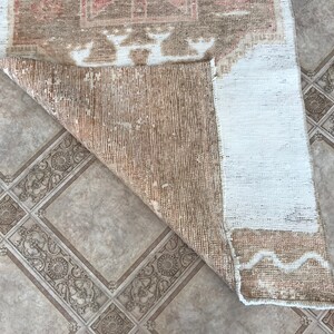 May include: The back side of a light brown rug with a white border. The rug has a woven pattern and is folded in half.