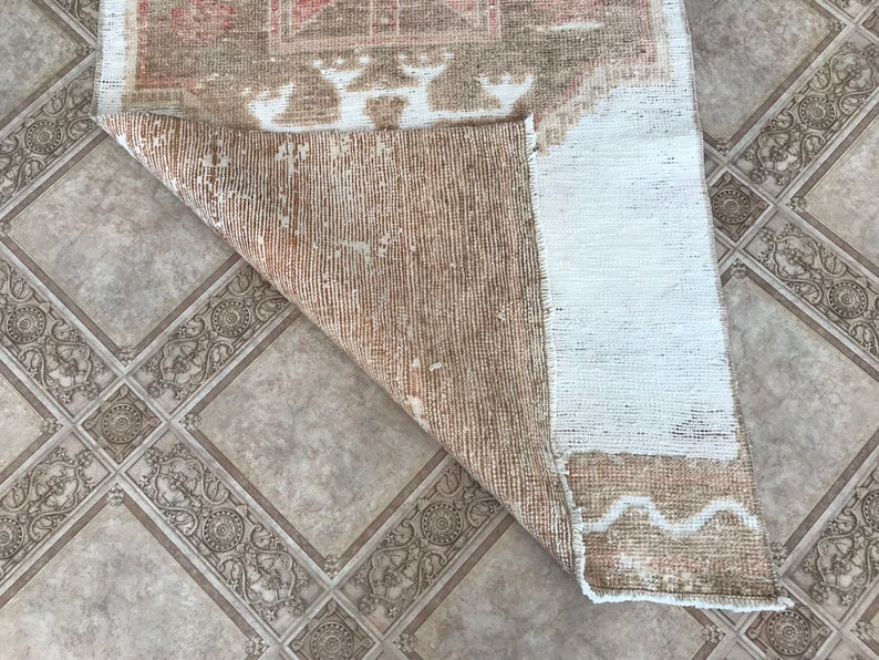 May include: The back side of a light brown rug with a white border. The rug has a woven pattern and is folded in half.