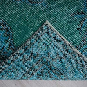 May include: Close-up of a teal and blue patterned rug with a frayed edge. The rug has a distressed look and is made of woven fabric.