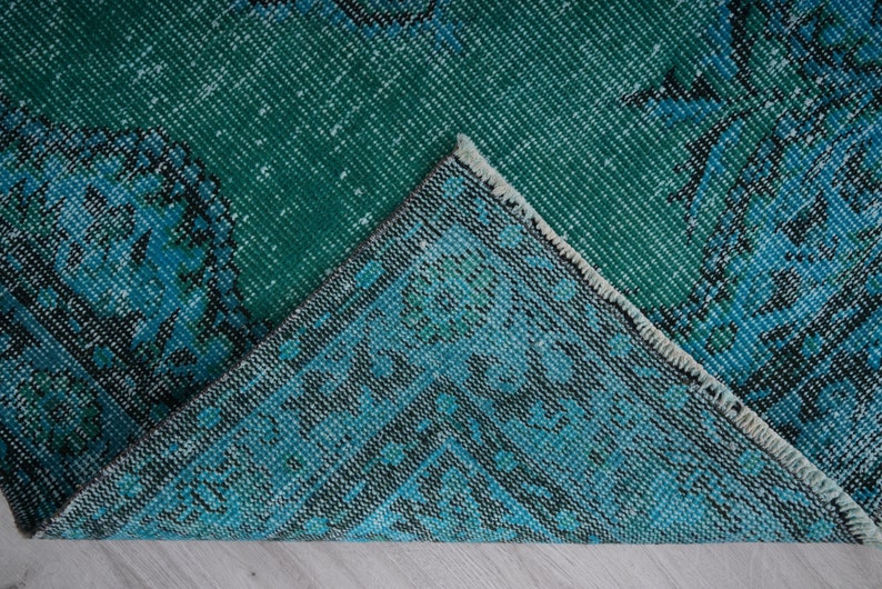 May include: Close-up of a teal and blue patterned rug with a frayed edge. The rug has a distressed look and is made of woven fabric.