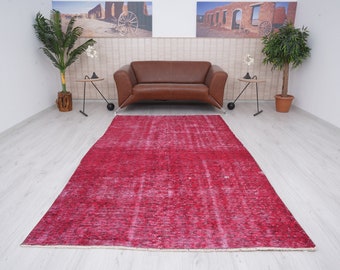 Könnte beinhalten: Ein roter Vintage-Teppich mit abgenutztem Look, der auf einem hellen Holzboden in einem Raum mit einem braunen Ledersofa und zwei Topfpflanzen liegt.